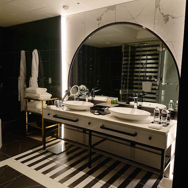 シャワールームの中の大きな半円形の鏡のついた洗面台。白と黒の基調で洗面ボウルが２つある。