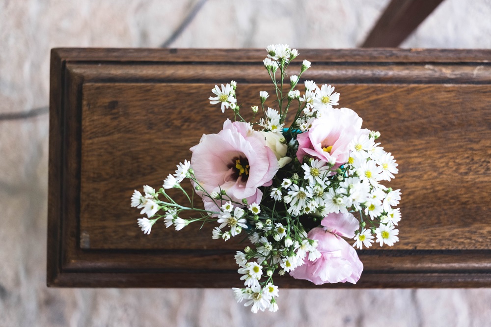 茶色い棺の上に大きなピンクの花と小さい白い花が置かれている