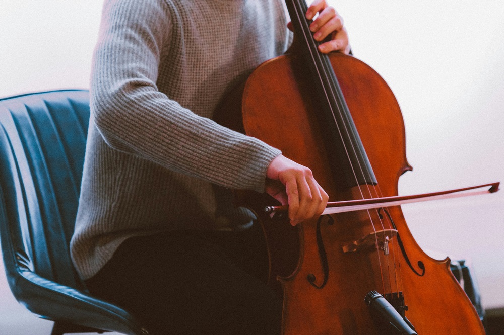 茶色のバイオリンを弾く灰色のセーターを着た男